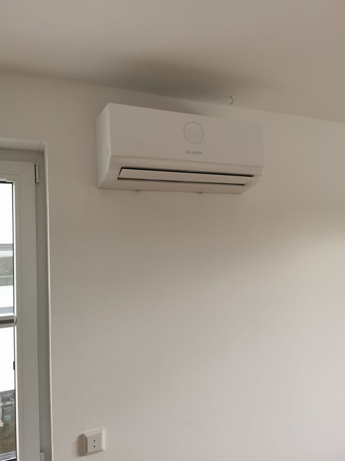 Wandmontiertes Innengerät einer Bosch-Klimaanlage, dezent oberhalb eines Fensters installiert, bereit zur Raumkühlung oder -heizung.